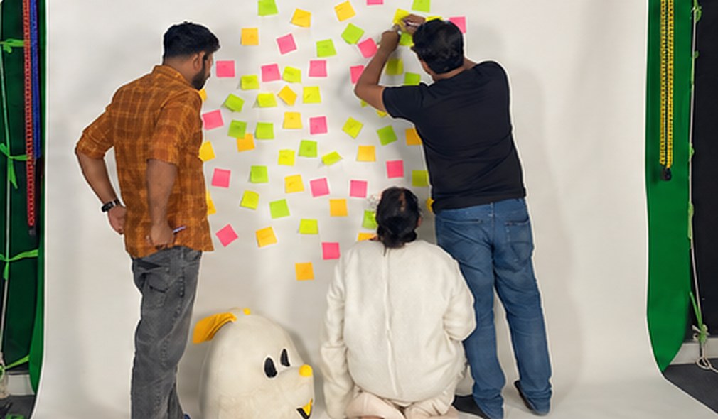 The team brainstorming at a wall covered in sticky notes, with the rabbit mascot head nearby